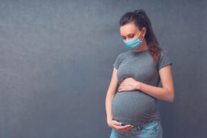 pregnant woman wearing mask on grey background 