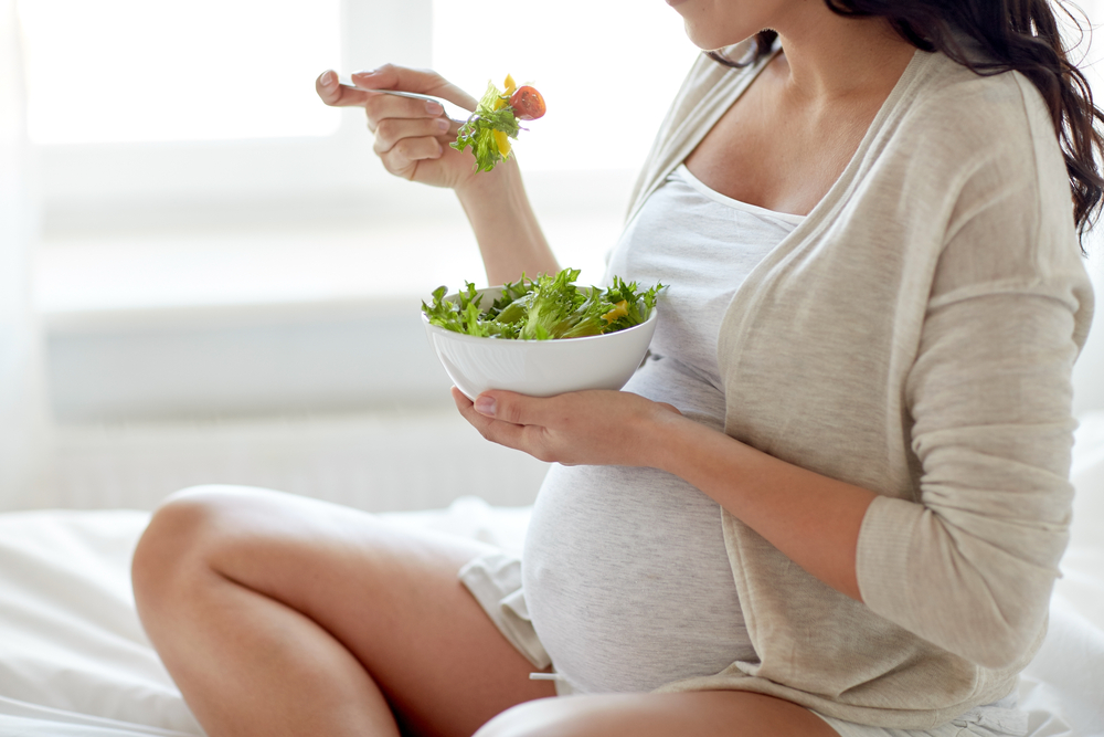 Close up of pregnant woman eating vegetable salad for in bed