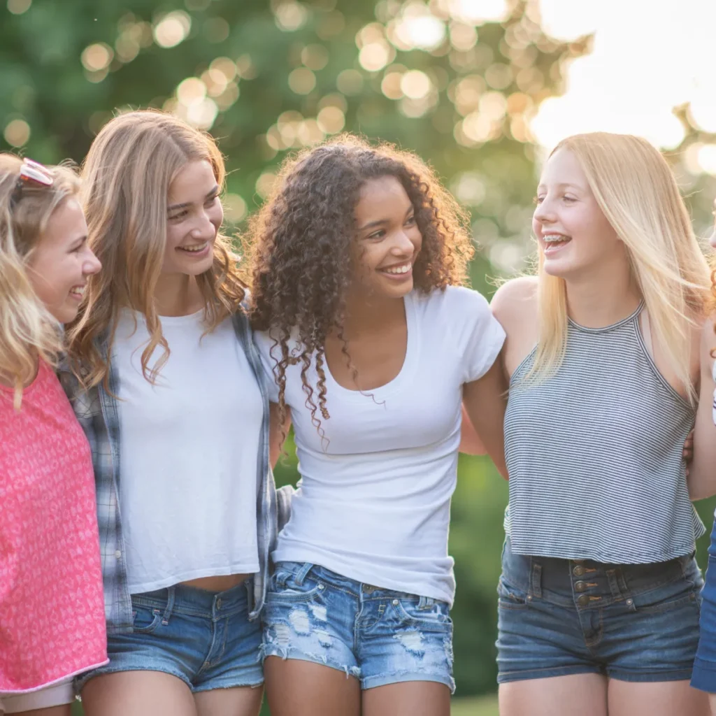Four diverse teenage girls smiling and laughing together outdoors.