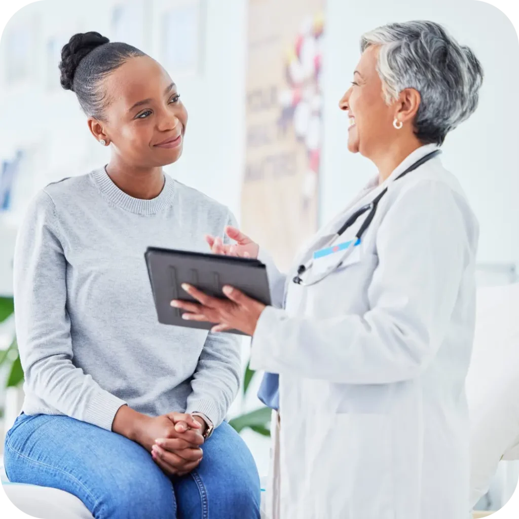 A smiling doctor discusses information on a tablet with a young female patient during a consultation.