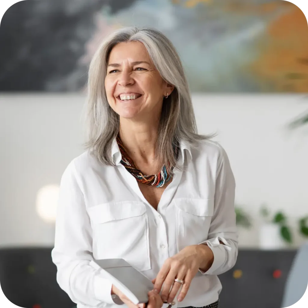 A smiling female practitioner with grey hair and a white shirt holding a tablet.