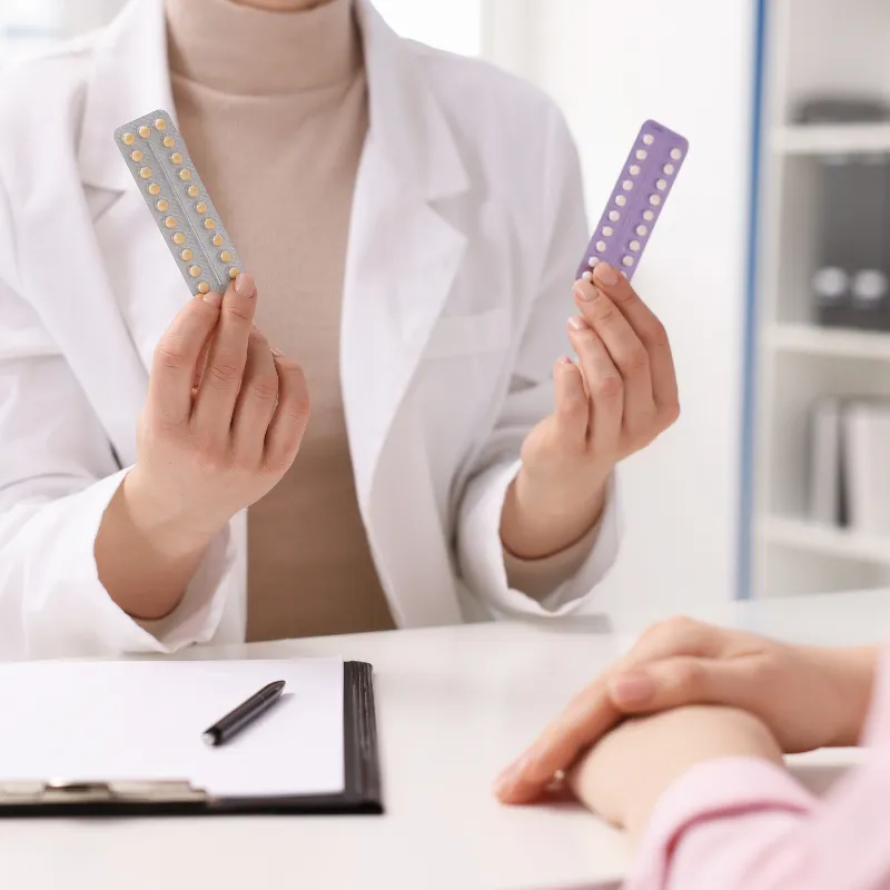 A doctor holds up two different birth control pill blister packs during a patient consultation.