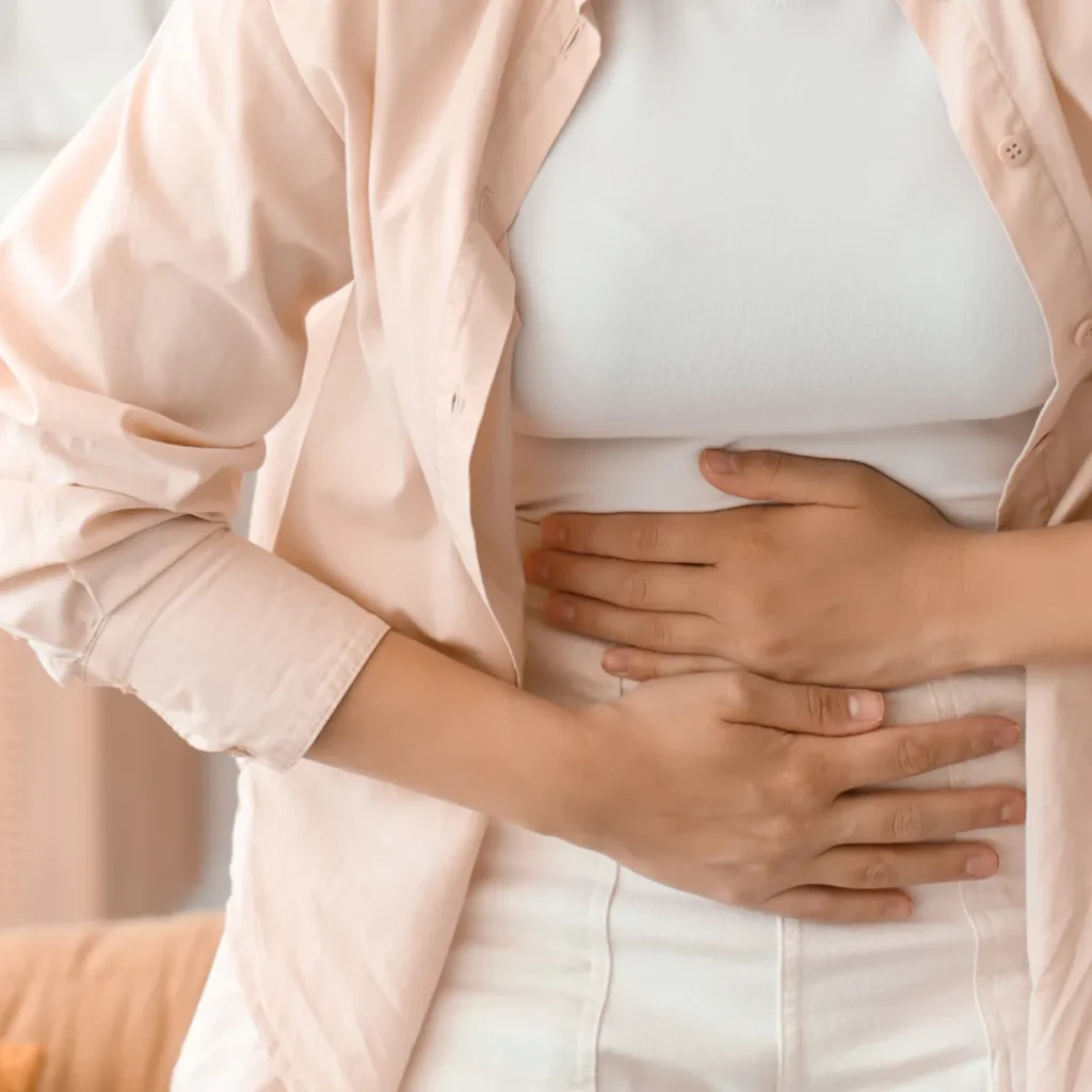 A woman holding her lower abdomen with both hands, representing pelvic pain or discomfort.
