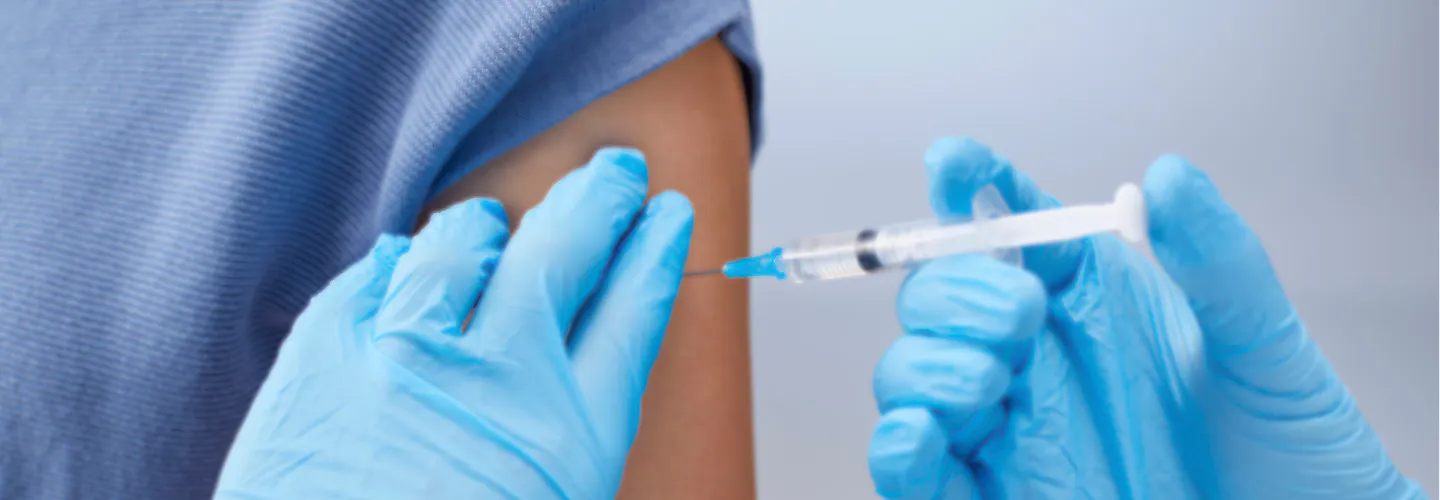 A healthcare provider in blue gloves administers a vaccine into a patient's upper arm.