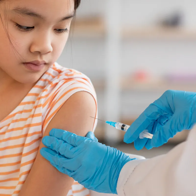 A young girl receives a vaccine injection in her arm from a healthcare provider.