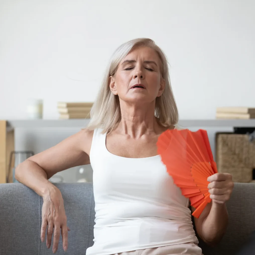 A middle-aged woman uses an orange hand fan to cool herself during a menopause hot flash.