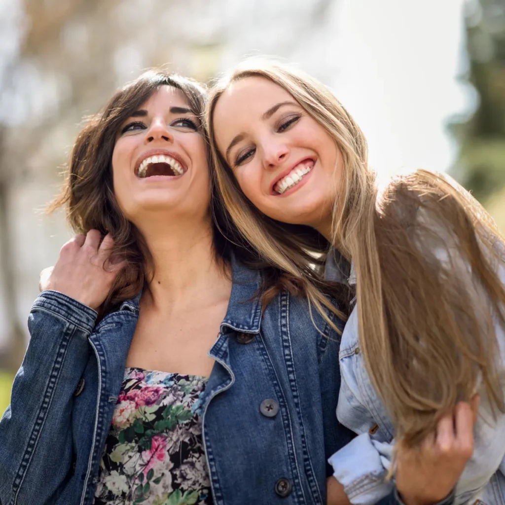 Two young women smiling and laughing together outdoors.