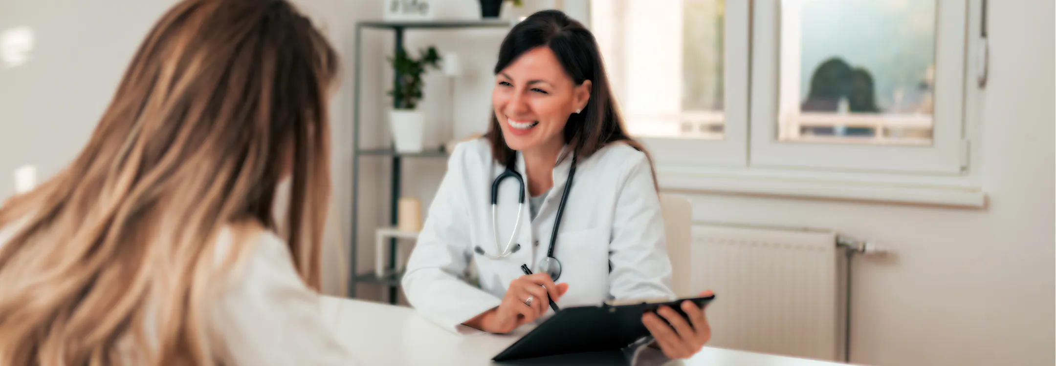 A smiling female doctor consults with a patient in a bright medical office.