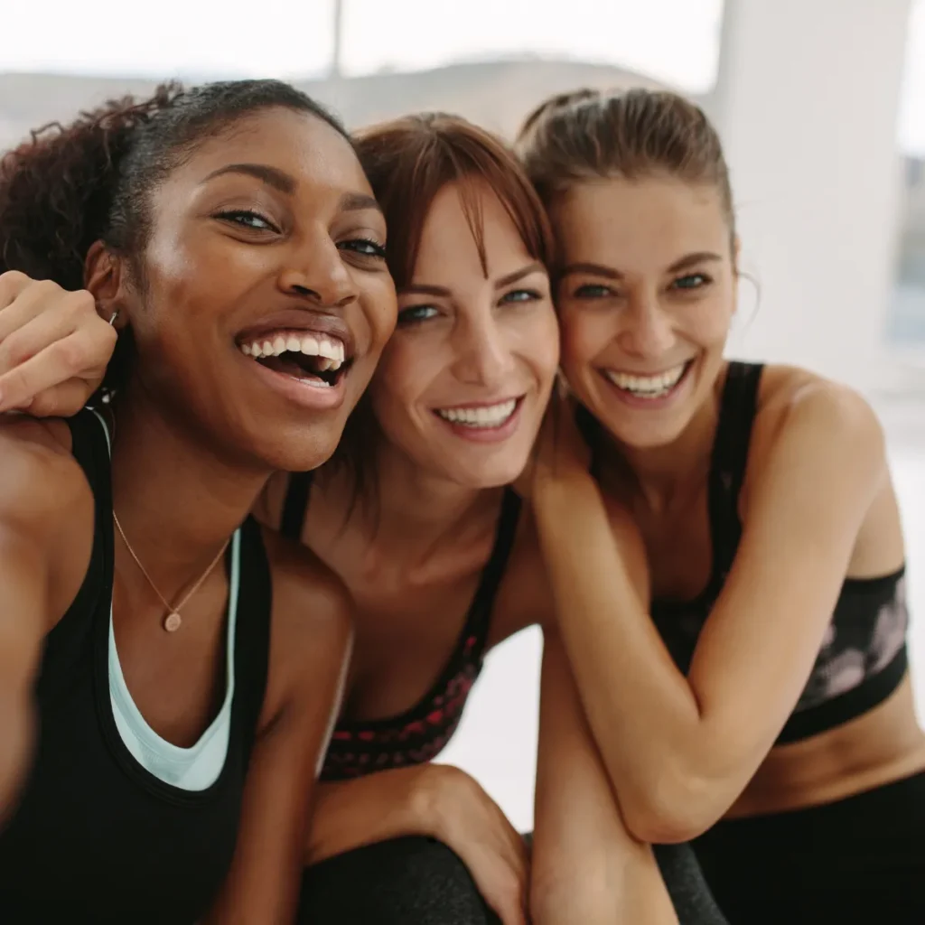 Three diverse, smiling women in athletic wear posing closely together.