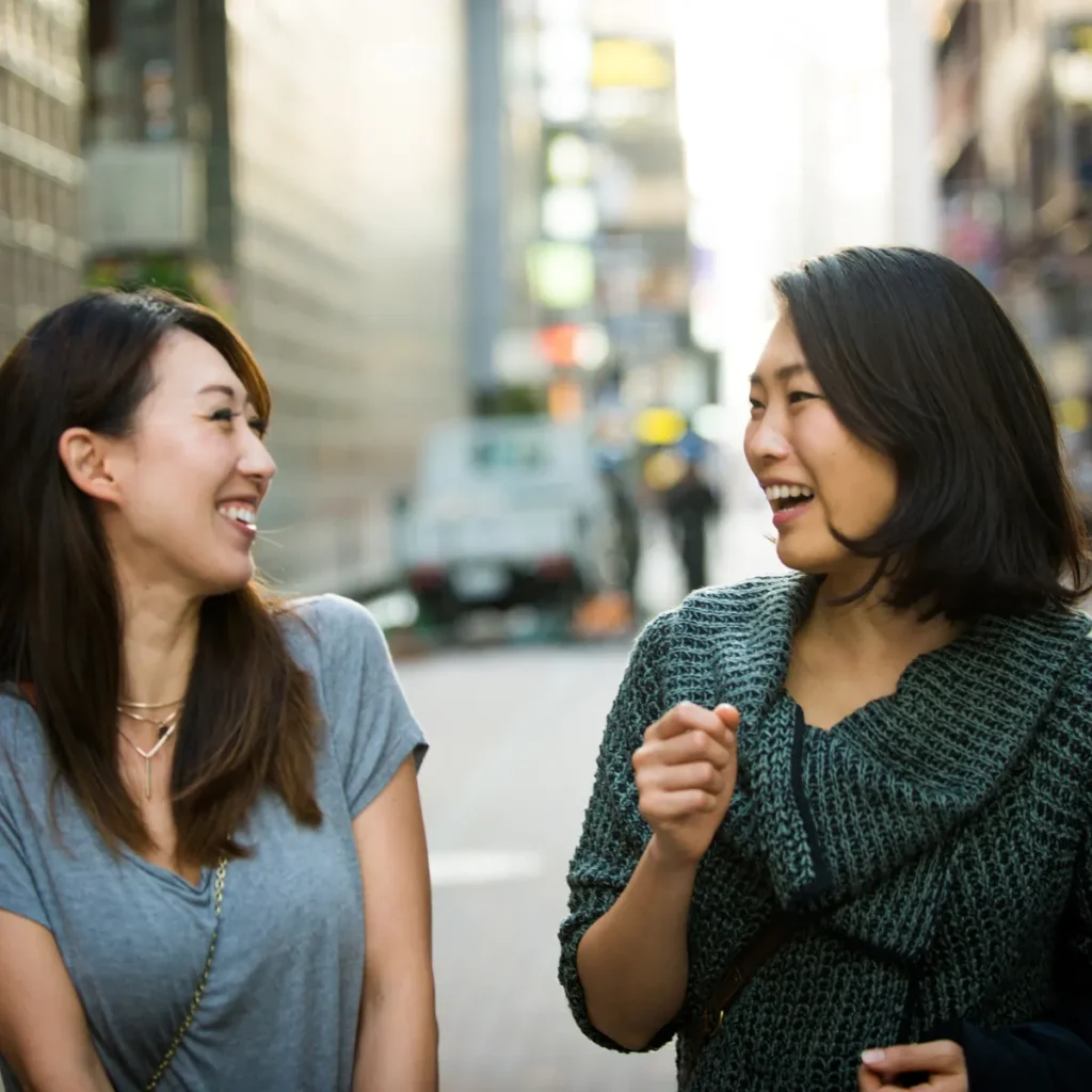 Two happy women laughing and talking together on a city street.