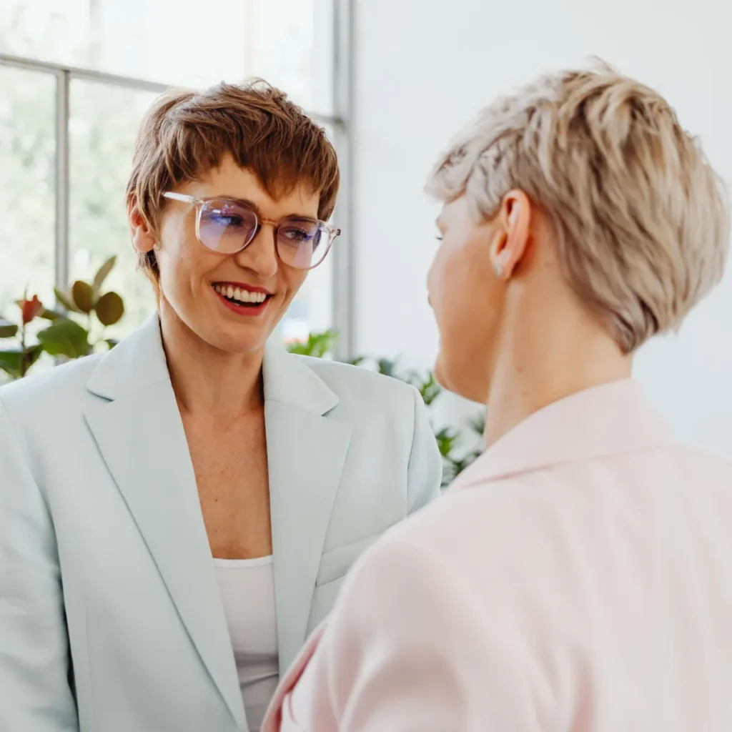 A smiling doctor in a light blue blazer speaks warmly with a patient during a consultation.