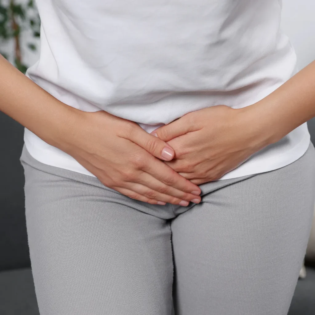 A woman holding her lower abdomen with both hands, representing pelvic pain or menstrual cramps.