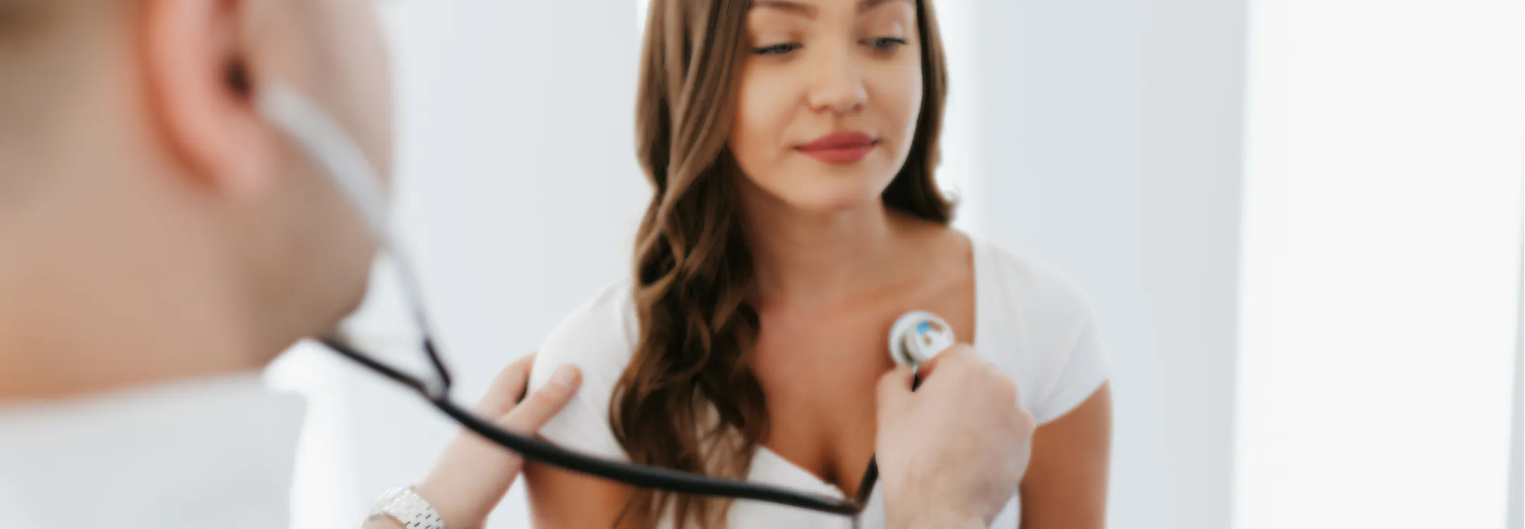 A doctor uses a stethoscope to listen to a female patient's heartbeat during a medical exam.