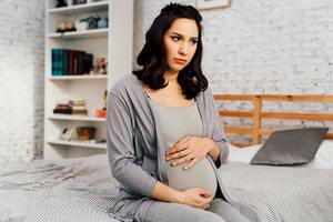 pregnant woman sitting on bed concerned