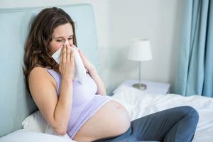 pregnant woman blowing her nose in bed